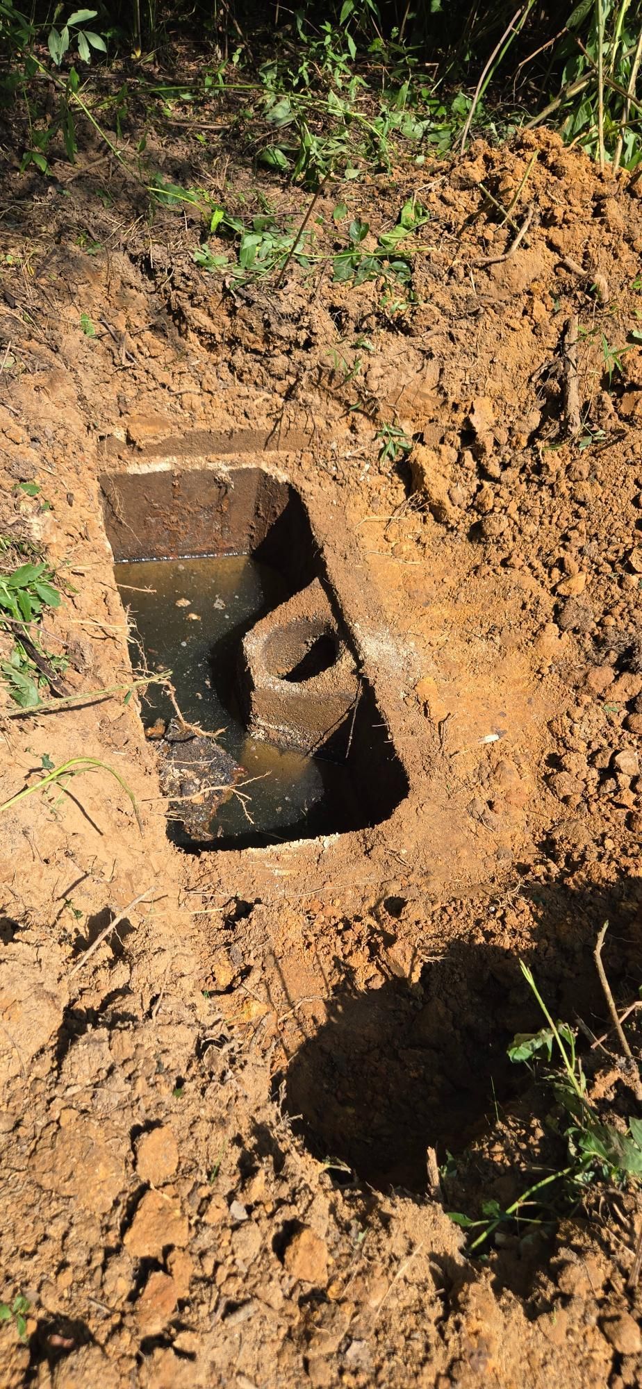 A rectangular concrete structure is partially buried in brown soil. 