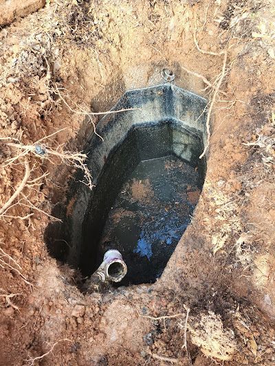 An oblong black tank partially buried in brown dirt, with a silver pipe protruding from it.