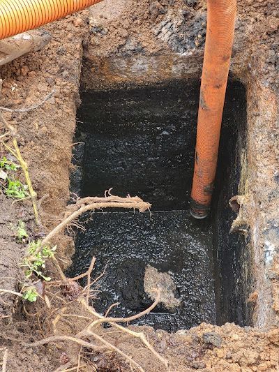 A rectangular hole in the ground filled with dark liquid, with an orange hose inserted. Soil surrounds the hole.