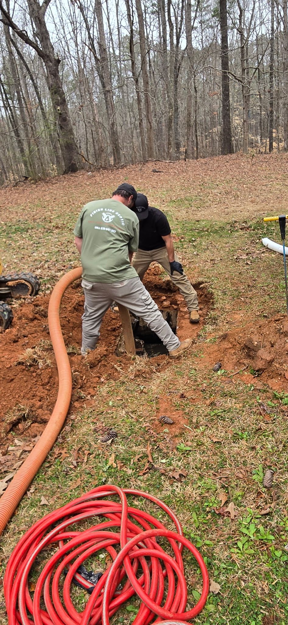 Two men digging a hole in a yard, with an orange hose connected. 