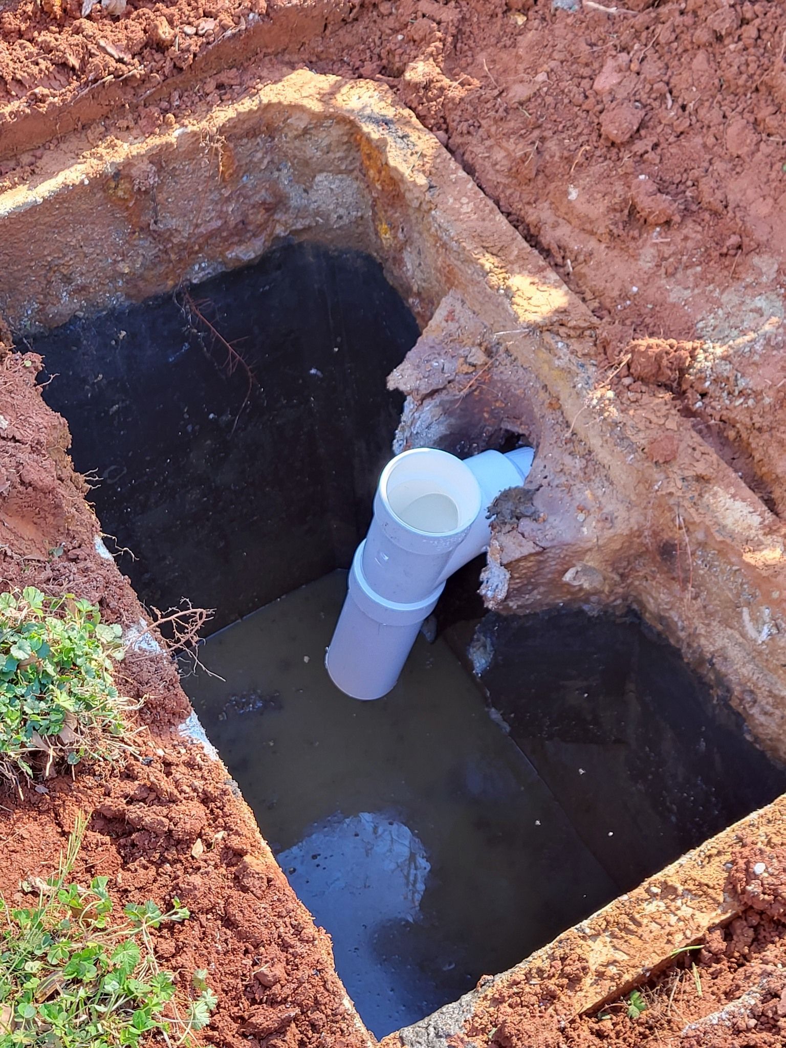 A rectangular hole in the ground filled with dark water, with a white PVC pipe system installed inside.