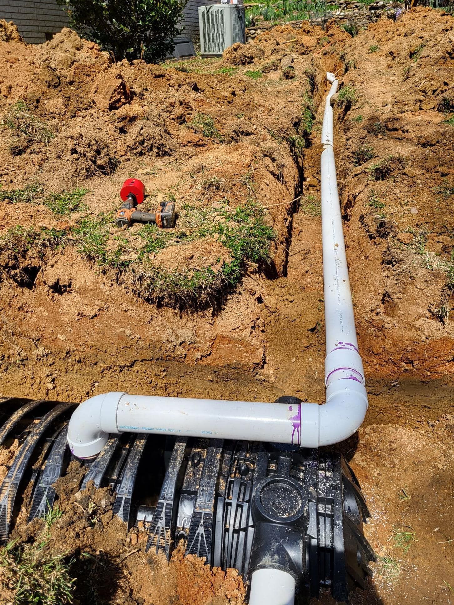 A white pipe drainage system connected to a black tank in a dirt trench.