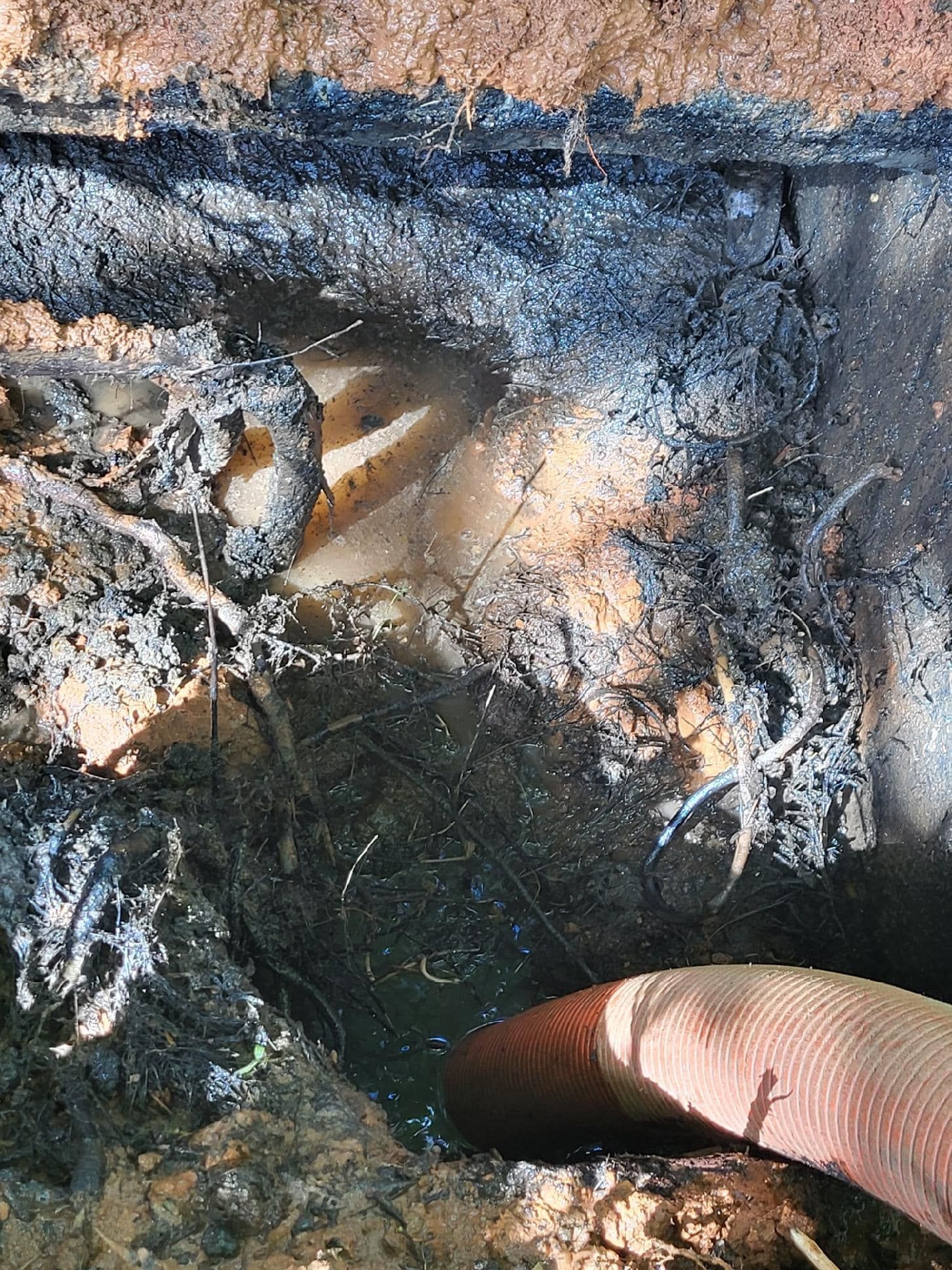 Open pit with water and debris, a hose is visible at the bottom, likely for pumping.