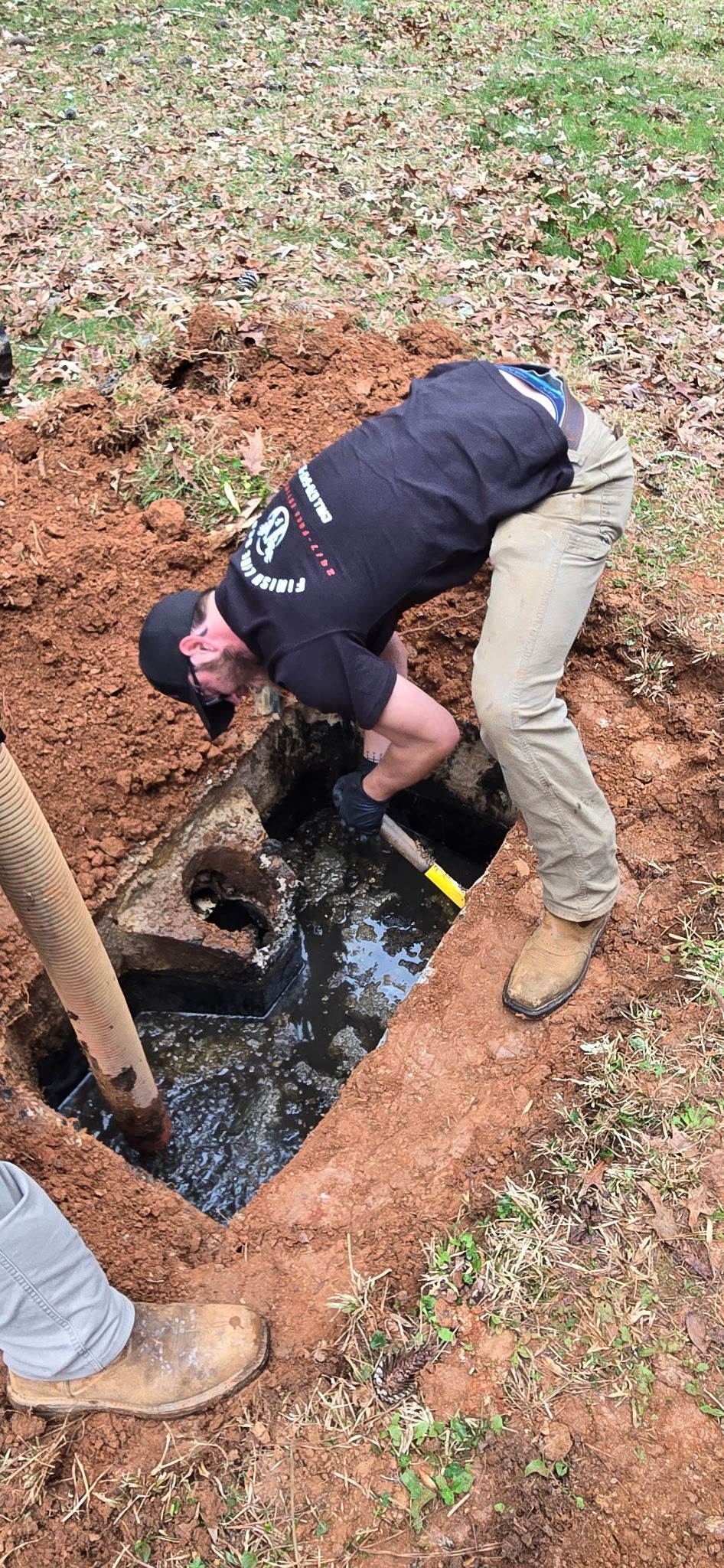 A person digging in a rectangular hole, possibly a septic tank, filled with water. T