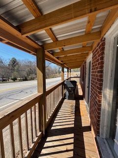 A covered wooden porch with a metal roof. The porch overlooks a road. Sunlight casts shadows on the wooden floor.