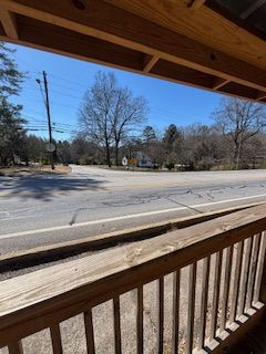 View from a wooden porch, overlooking a two-lane road and trees under a clear blue sky.