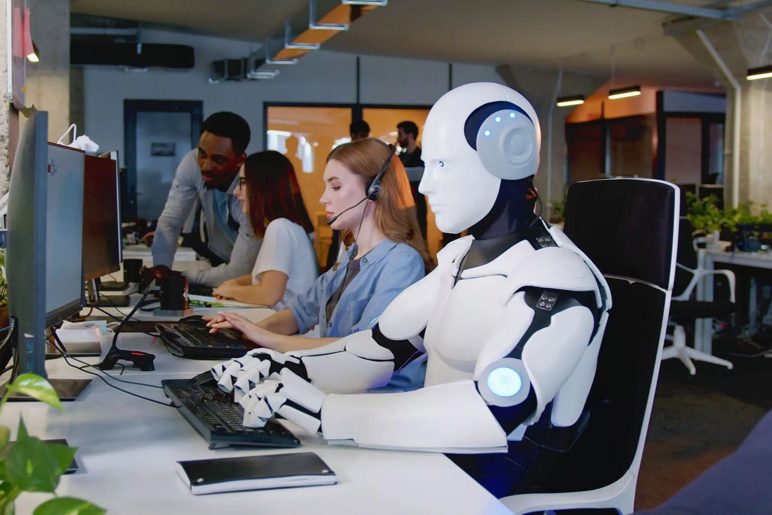 AI working at a computer in an office setting, with human colleagues nearby.