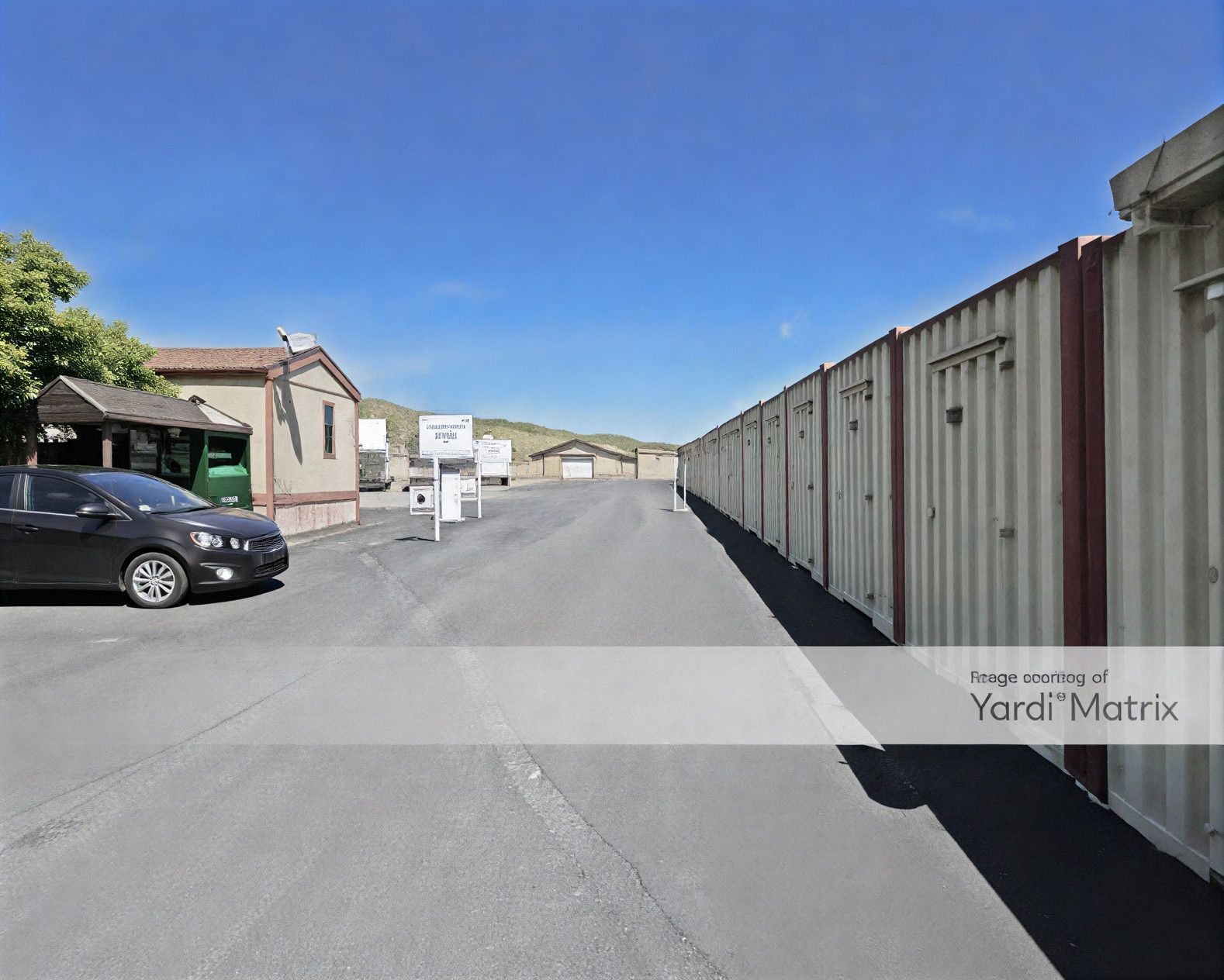 Storage units along a paved drive with a car and office building.
