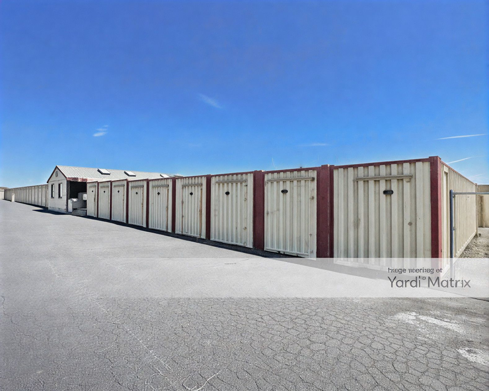 Storage units in a row, with gray metal doors and red trim, under a blue sky.