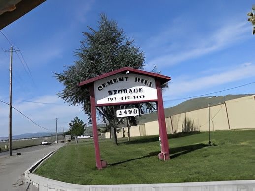 Sign for Cement Hill Storage, with phone number and address, in front of a green grassy area and storage units.