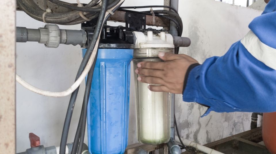 A person's hands changing a water filter, blue and clear filters are visible, indoors.