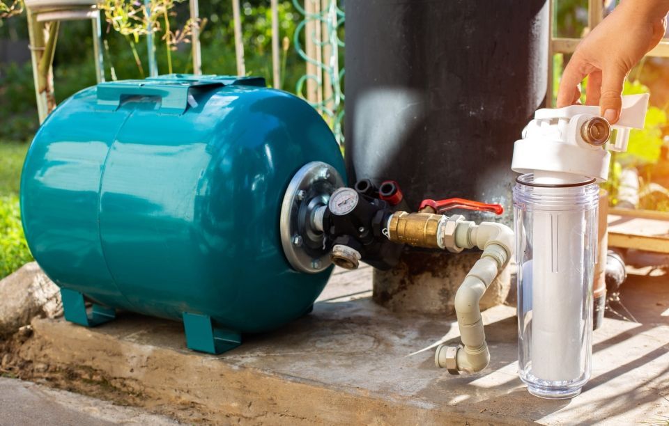 A person installs a water filter system, including a blue tank, outside on a concrete surface.