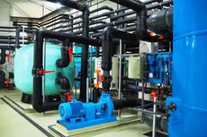 Water treatment plant equipment with blue tanks, pipes, and pumps, indoors.