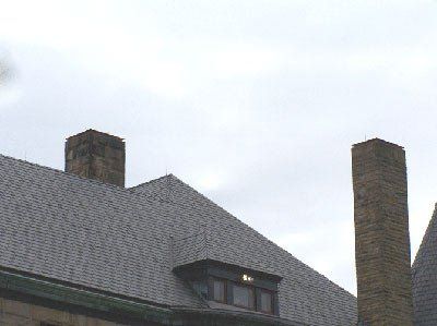 Gray rooftop with two brick chimneys against an overcast sky.