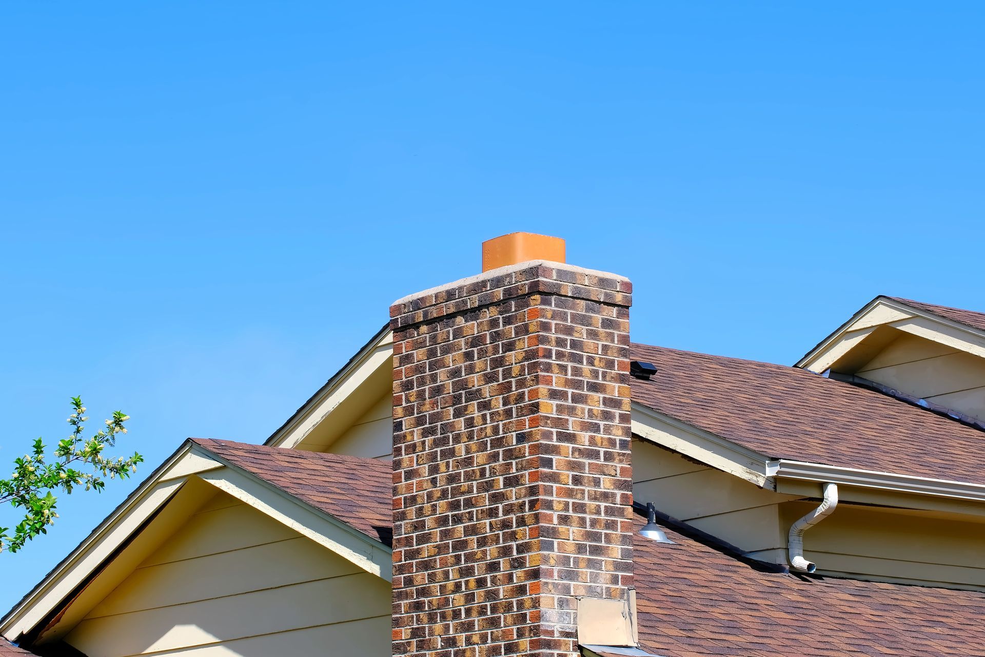 Chimney repair on house roof with fireplace vent, spring tree, and blue sky in background.