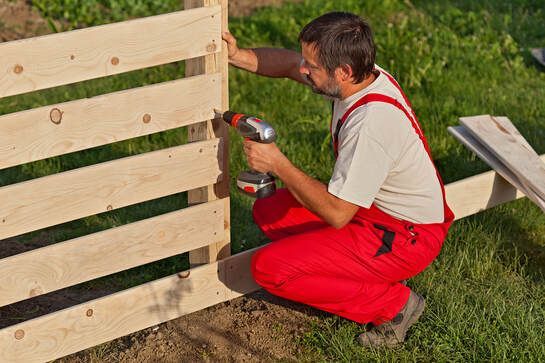 Fencing Contractor making a fence repair wearing red overalls and applying exterior weather resistant screws