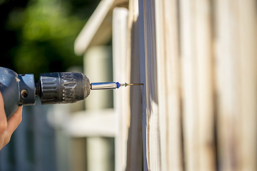 man attaching wood to a fence via zinc screw