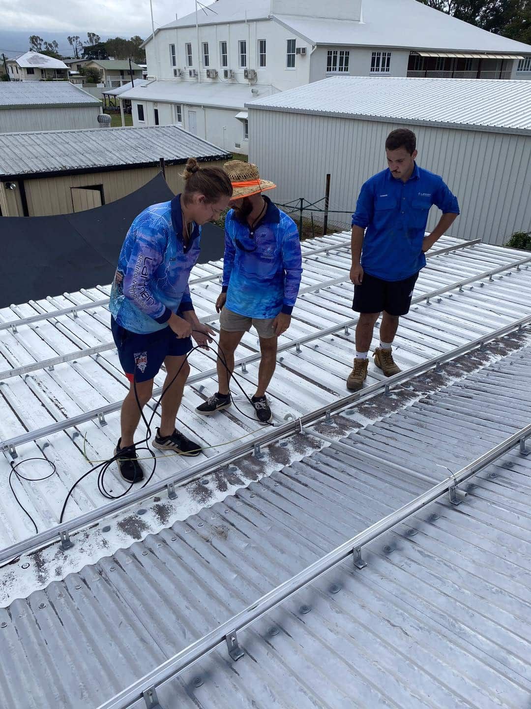 Three People on a Metal Roof, Likely Installing Something — Lahtinen Electrical & Refrigeration in Ingham, QLD