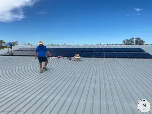 Men Installing Solar Panels on a Silver Metal Roof Under a Blue Sky — Lahtinen Electrical & Refrigeration in Ingham, QLD