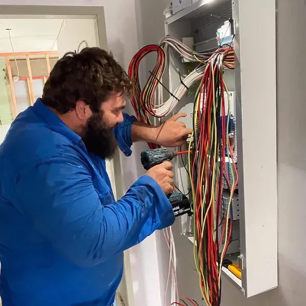 Electrician in Blue Shirt Using a Drill on Wiring in a Metal Cabinet — Lahtinen Electrical & Refrigeration in Ingham, QLD