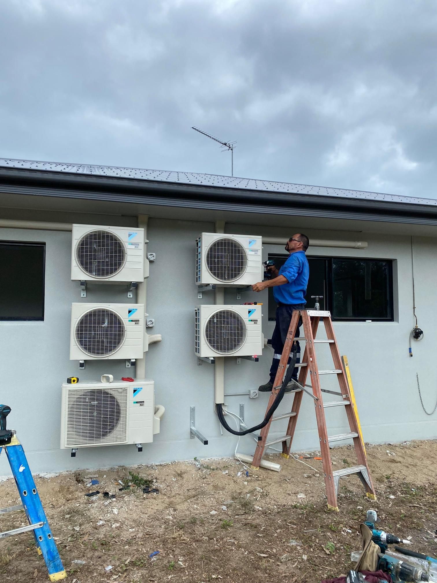 Man on ladder installing air conditioning units on a building's exterior.— Lahtinen Electrical & Refrigeration in Ingham, QLD