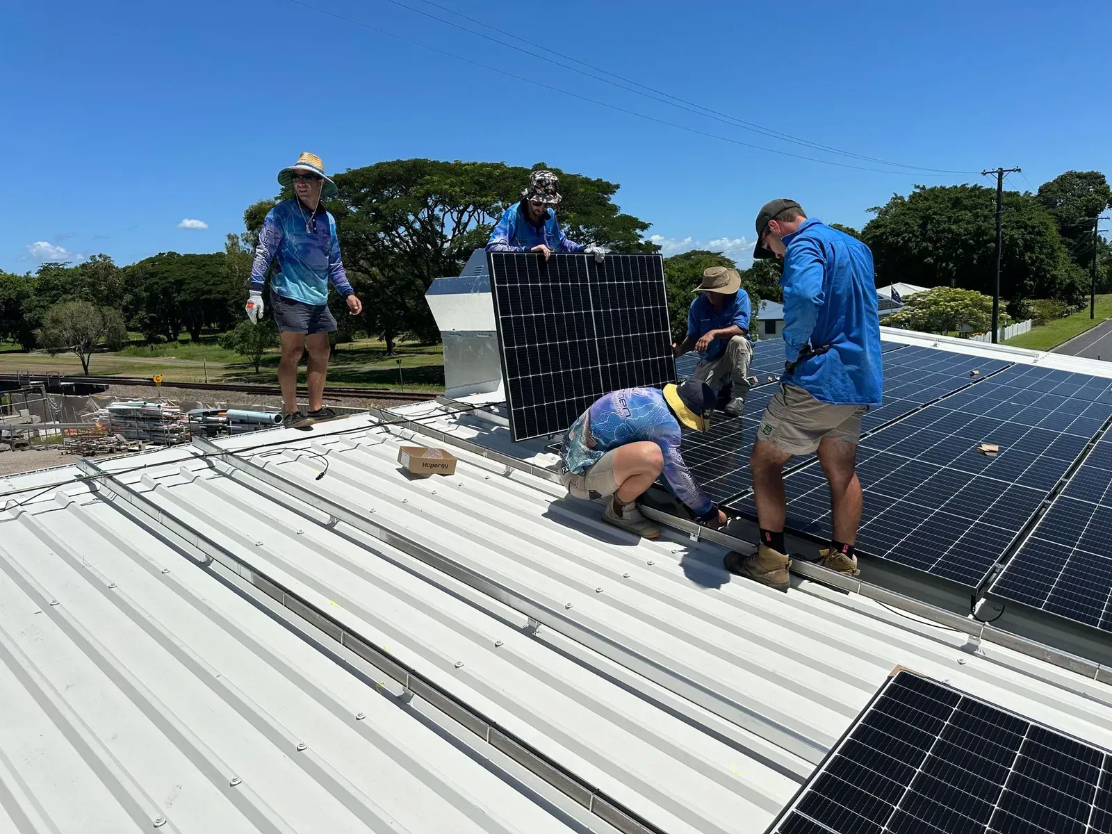 Workers Installing Solar Panels on a Rooftop Under a Sunny Sky — Lahtinen Electrical & Refrigeration in Ingham, QLD