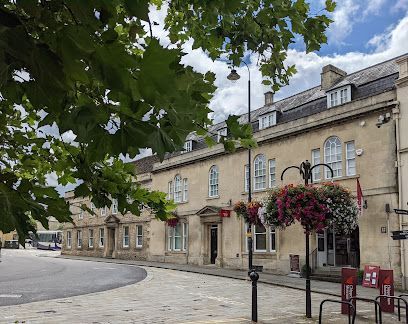 Quiet street with stone buildings, hanging flower baskets, and trees under a cloudy sky