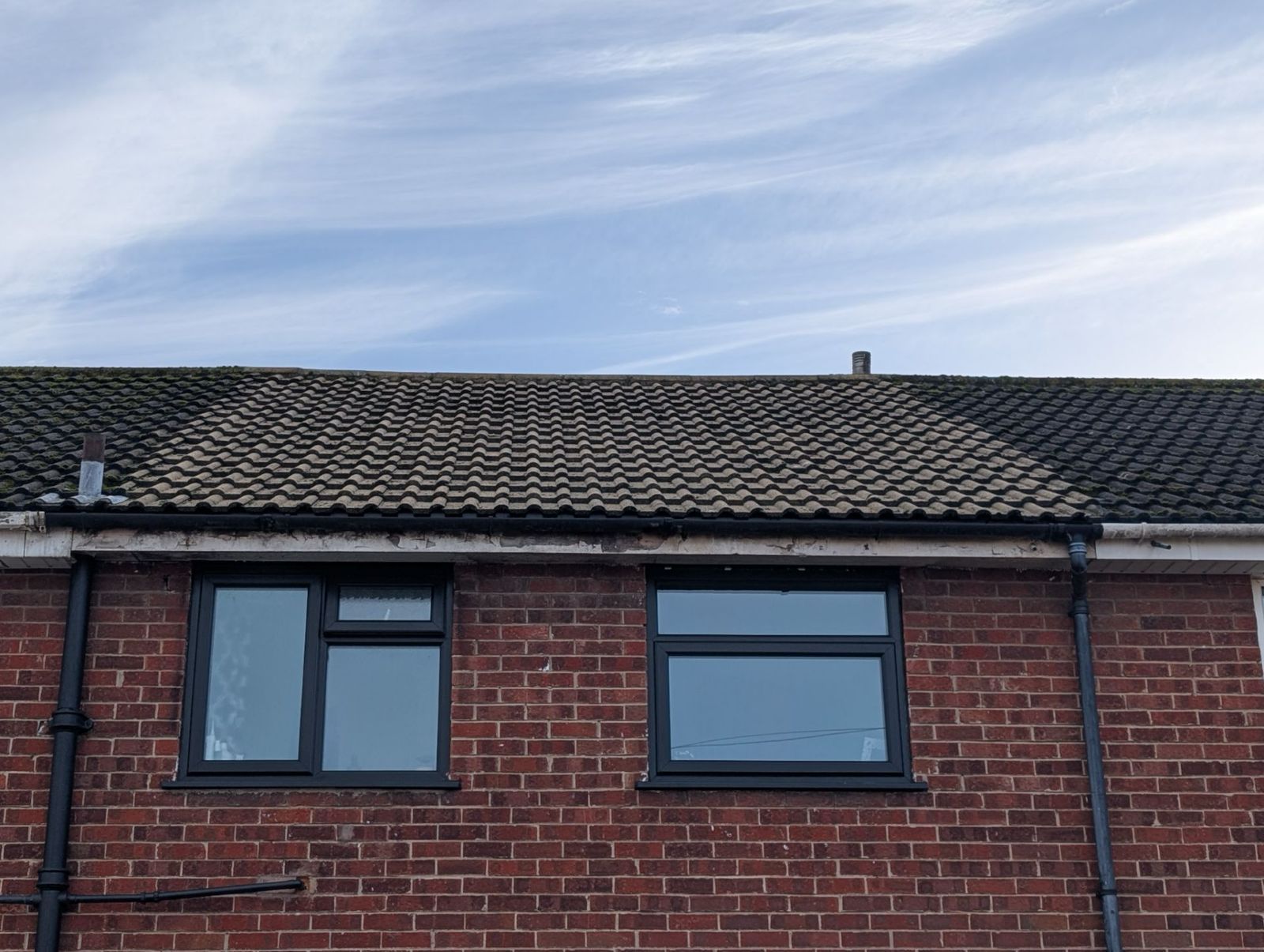 Brick house roofline with two upper windows under a cloudy sky