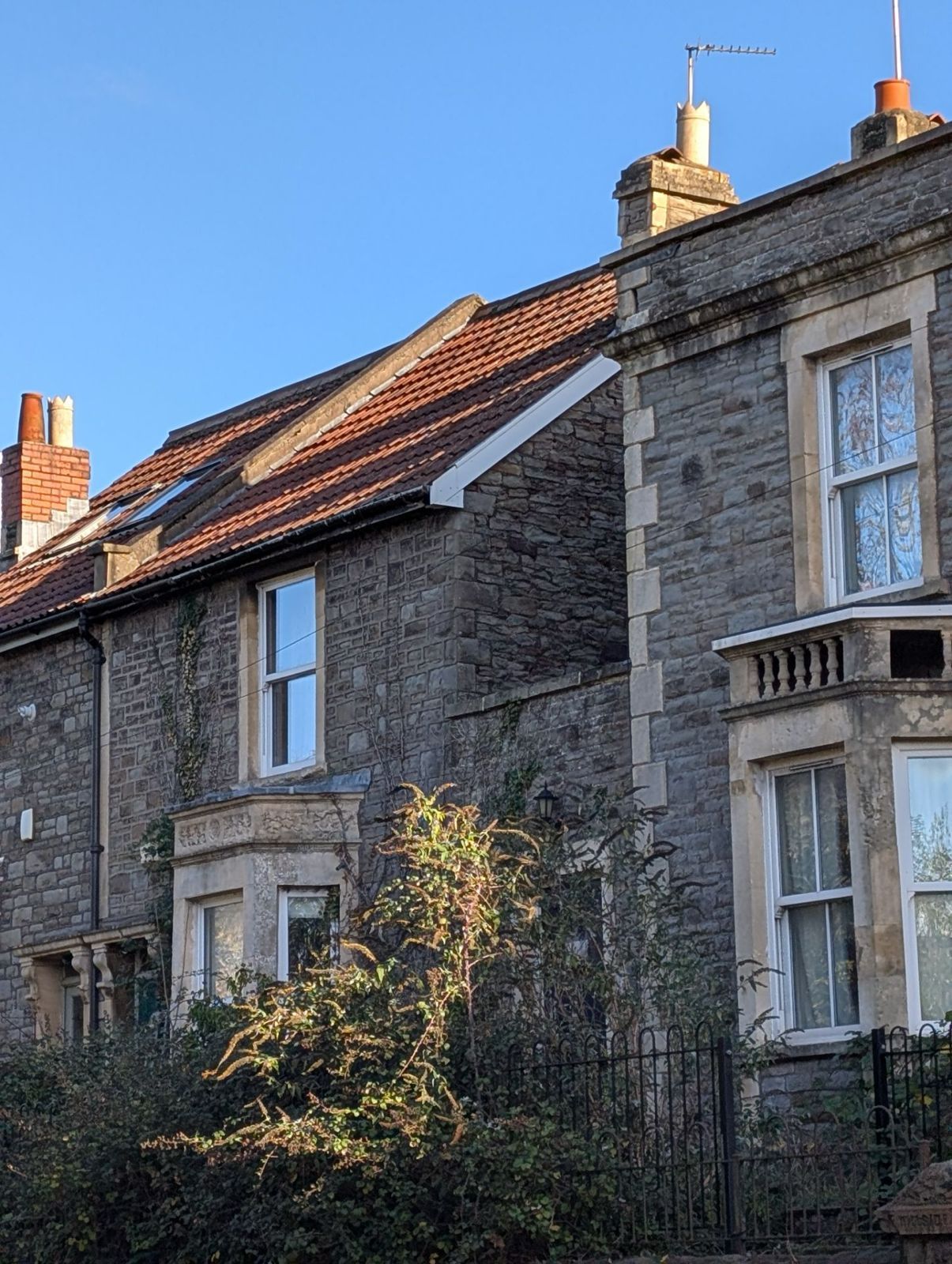 Sunlit stone row houses with red-tiled roofs and chimney stacks along a quiet street