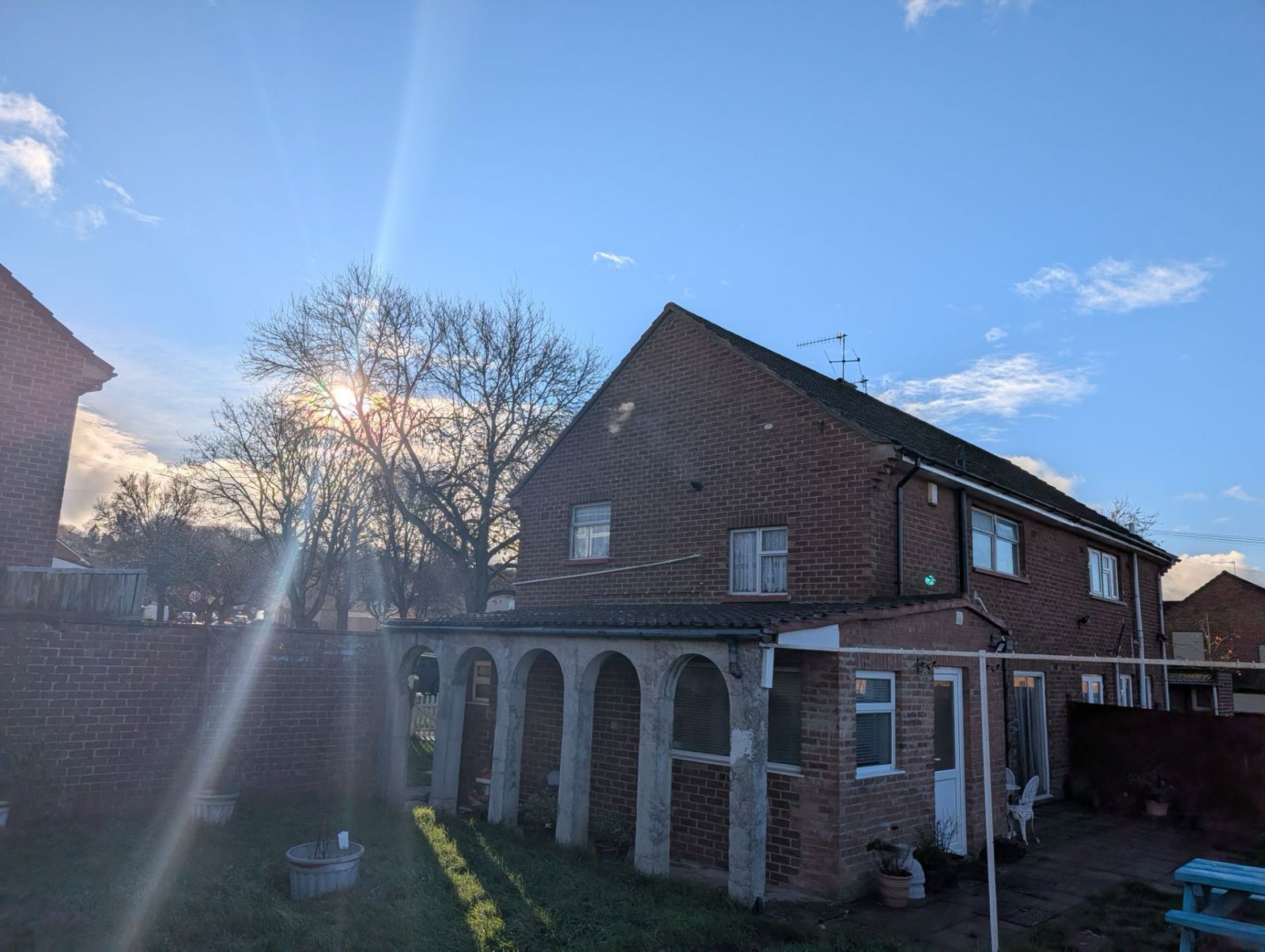 Sunlit brick house with arched porch and blue sky at dusk
