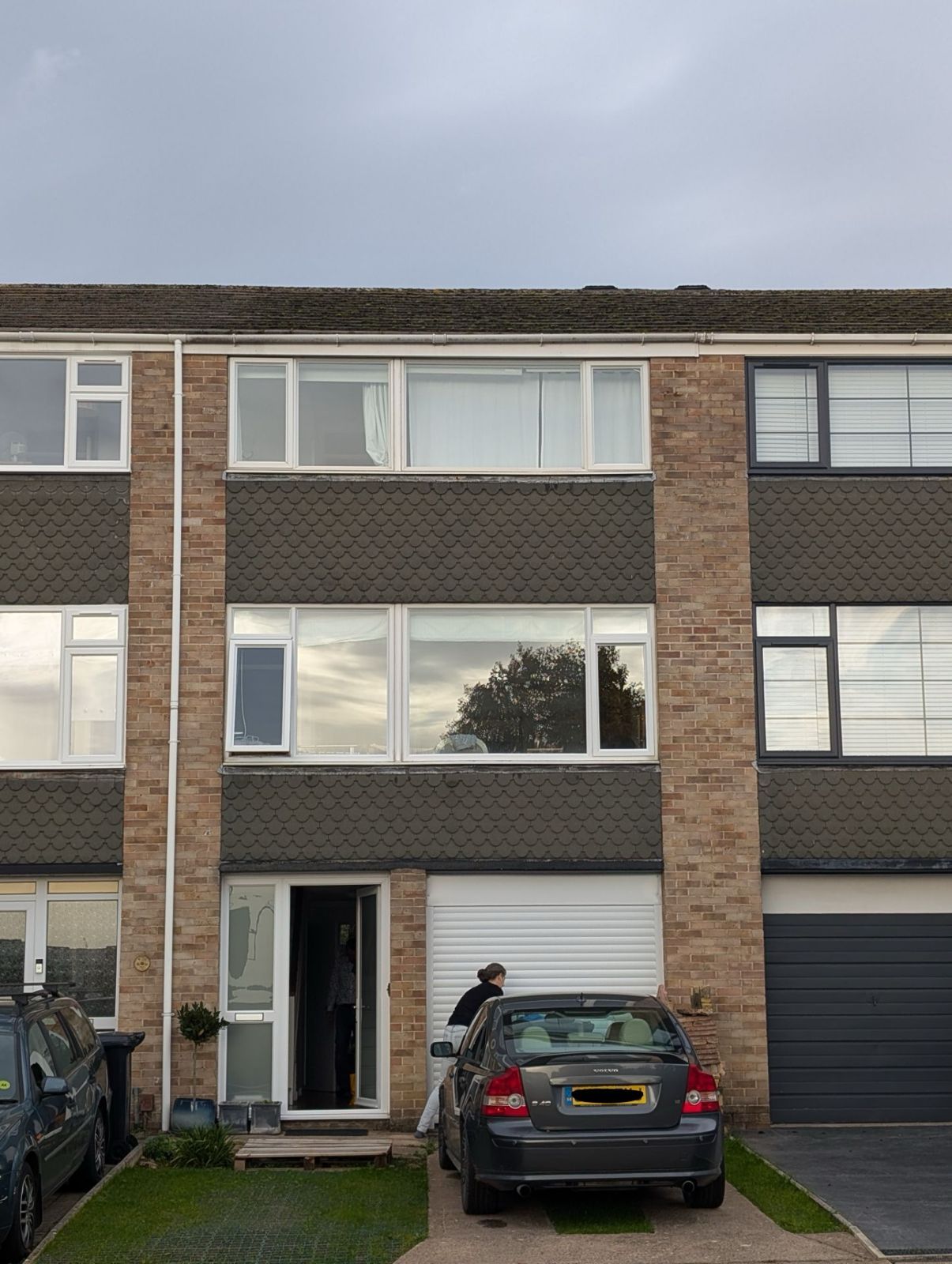 Three-story townhouse with a parked gray car and a person standing by the front door