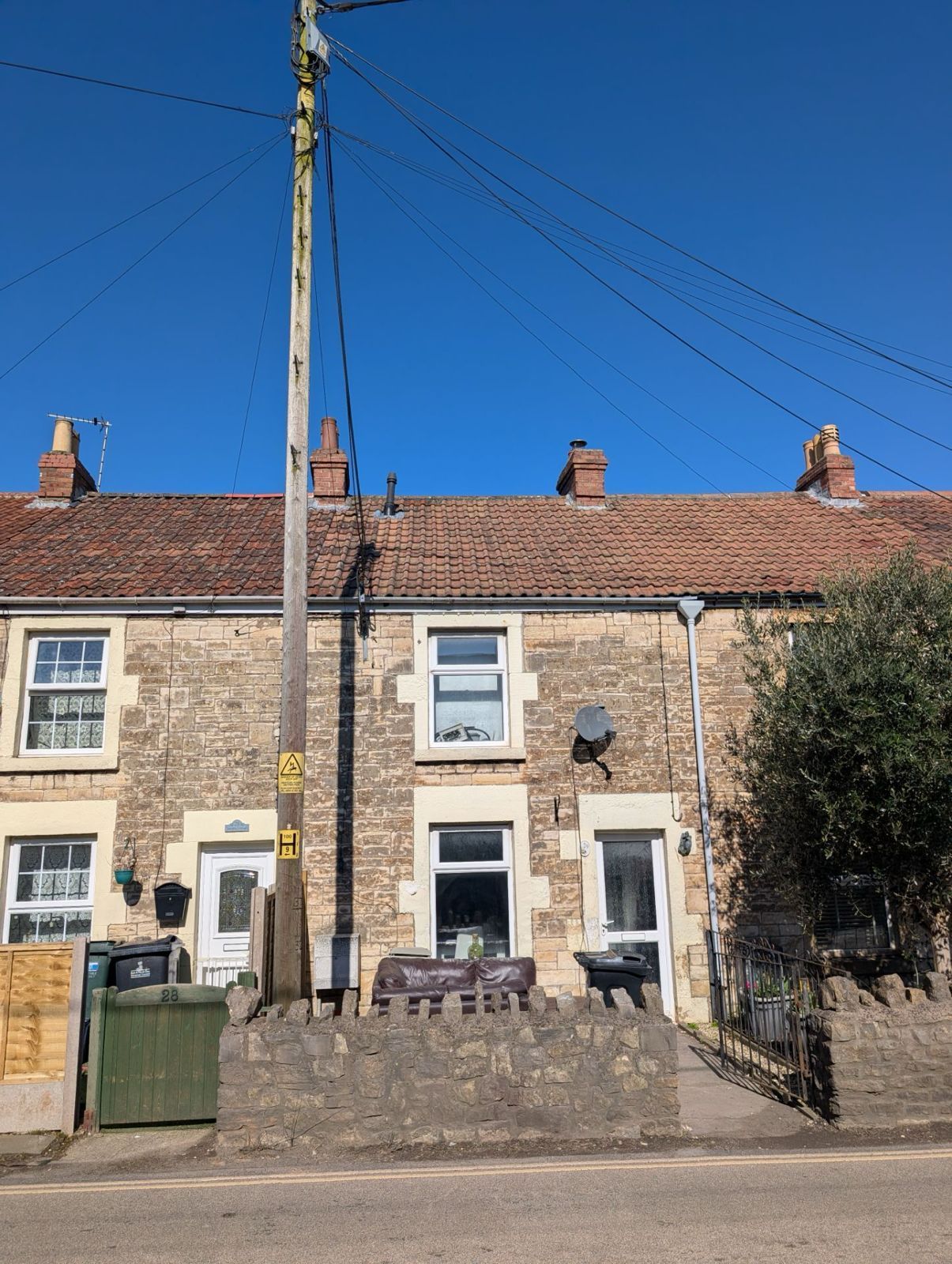 Row of stone cottages with a red-tiled roof under a clear blue sky, with a utility pole in front.