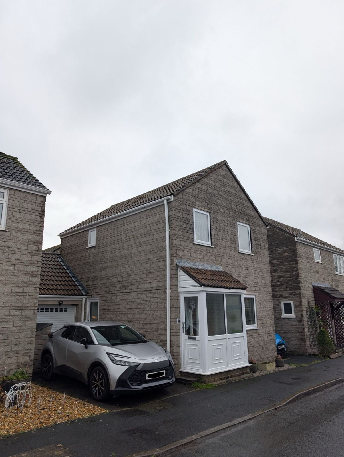 Two-story brick house on a wet street with a silver SUV parked beside it.