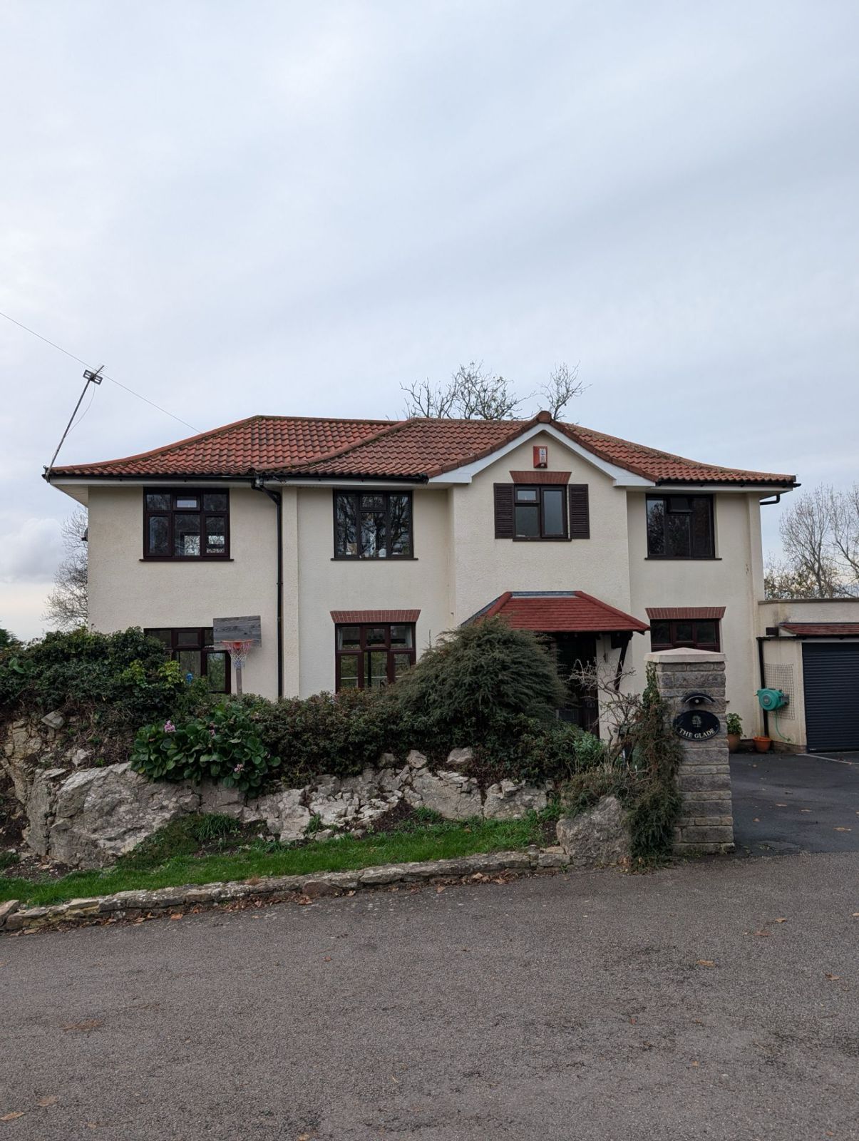 Two-story beige house with red-tile roof and small front garden under an overcast sky