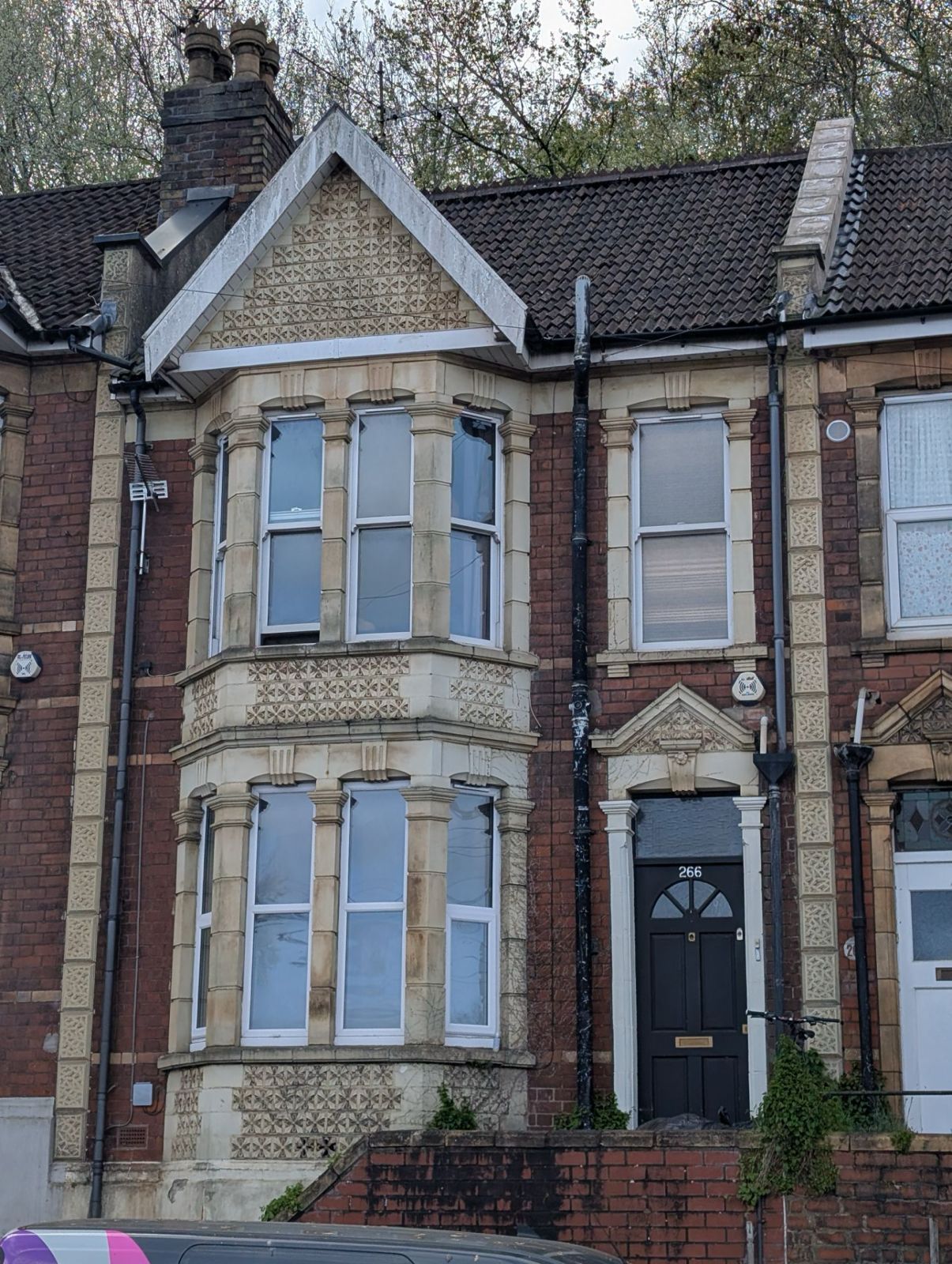 Victorian brick townhouse with bay windows, black front door, and steep slate roof