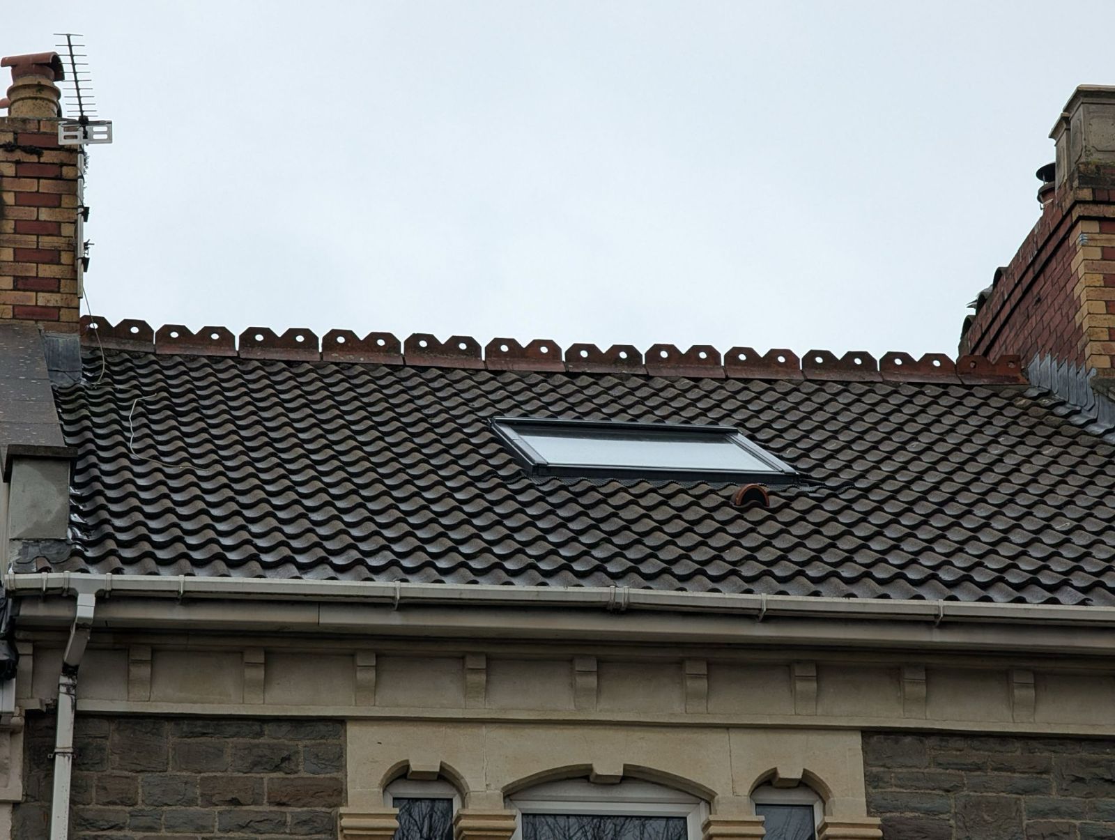 Old tiled roof with a skylight between brick chimneys under a pale sky