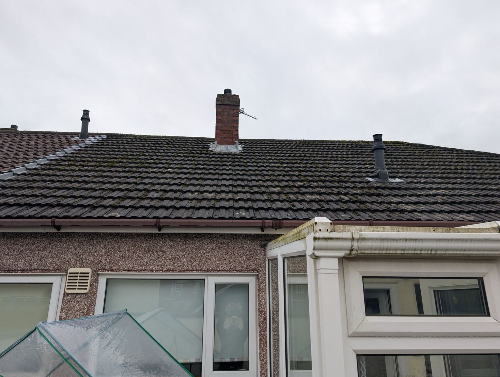 Rooftop with brick chimney and dormer windows above a house in cloudy weather