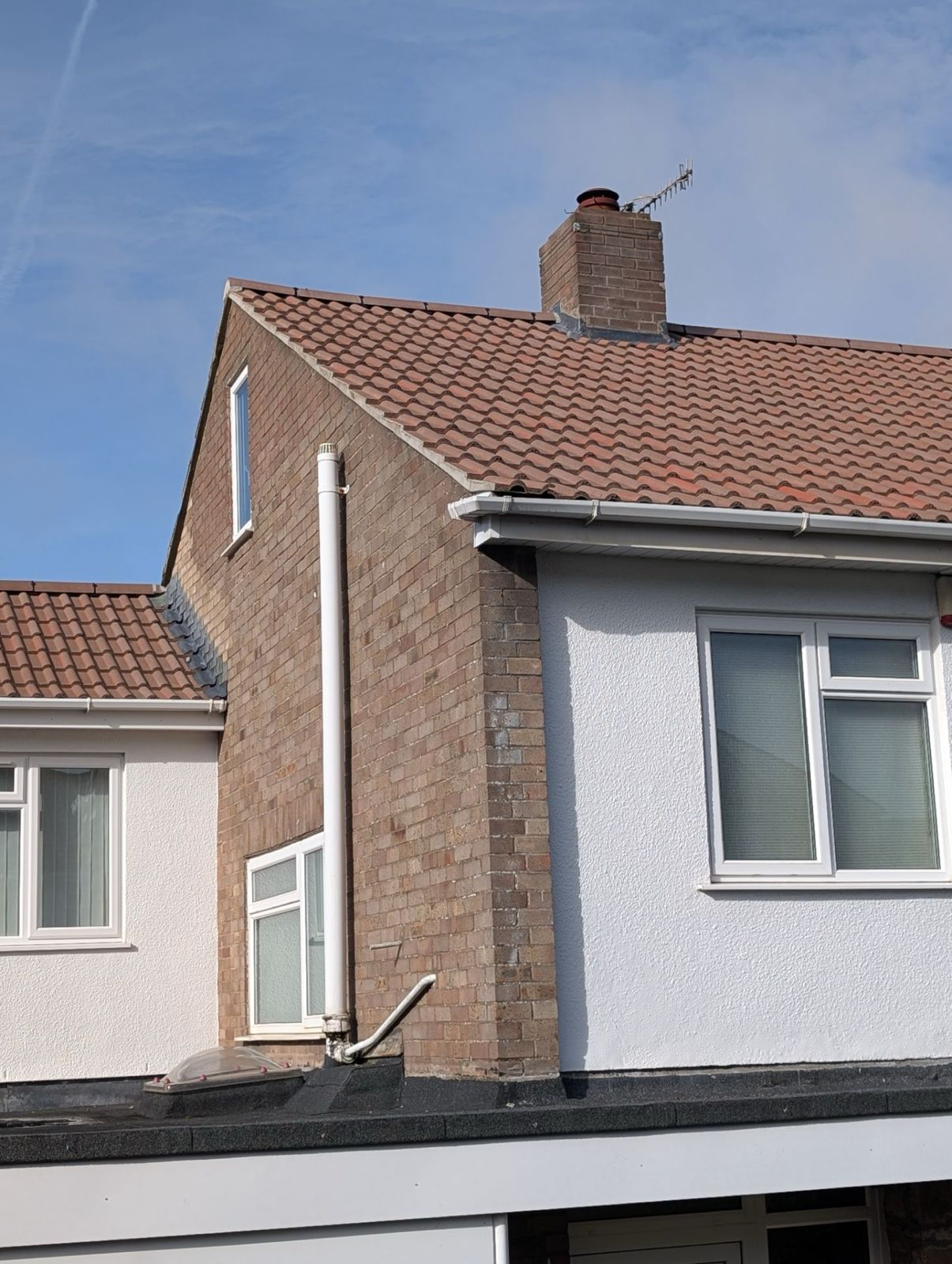 Two adjoining houses with white and brick facades, red tiled roofs, and a blue sky above.