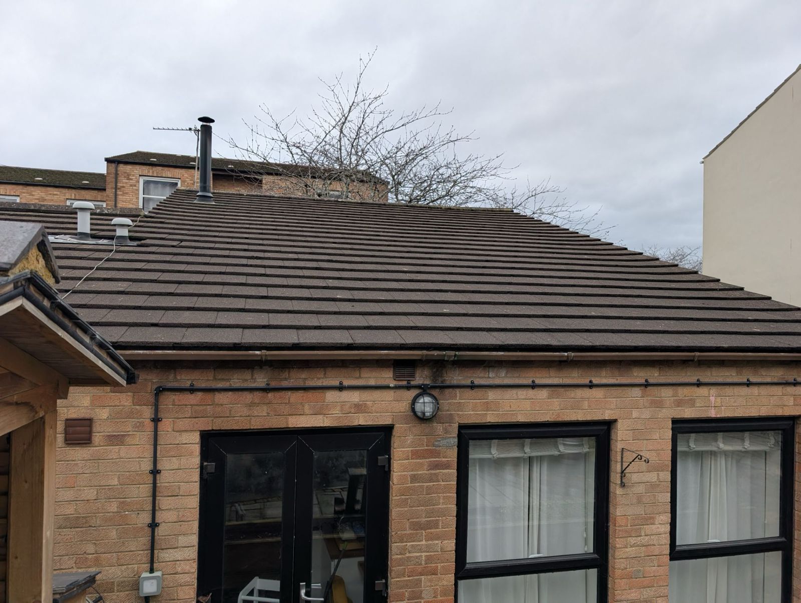 Brick house roof with dark shingles and two front windows under a cloudy sky