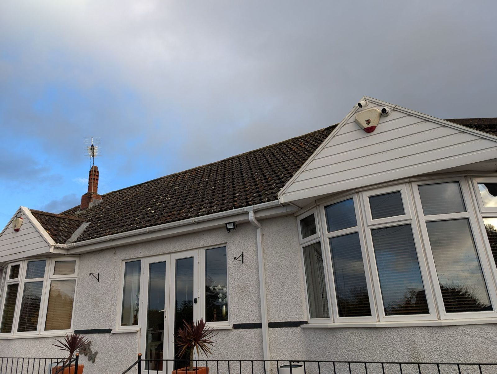 White bungalow with bay windows and a tiled roof under a cloudy sky