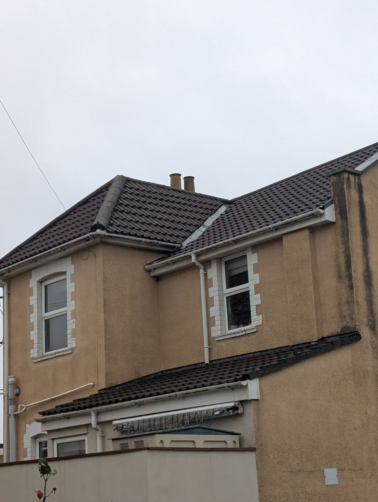 Two-story beige house with dark tiled roof and white-trimmed windows under a gray sky