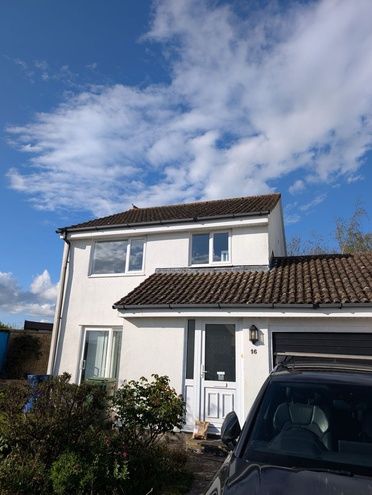 White two-story house with a tiled roof under a blue sky, with a car parked in front
