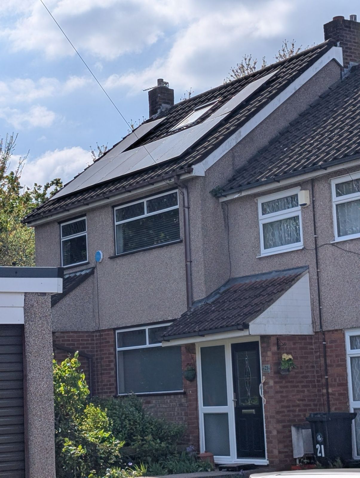 Suburban brick house with solar panels on a sloped roof and a small front garden