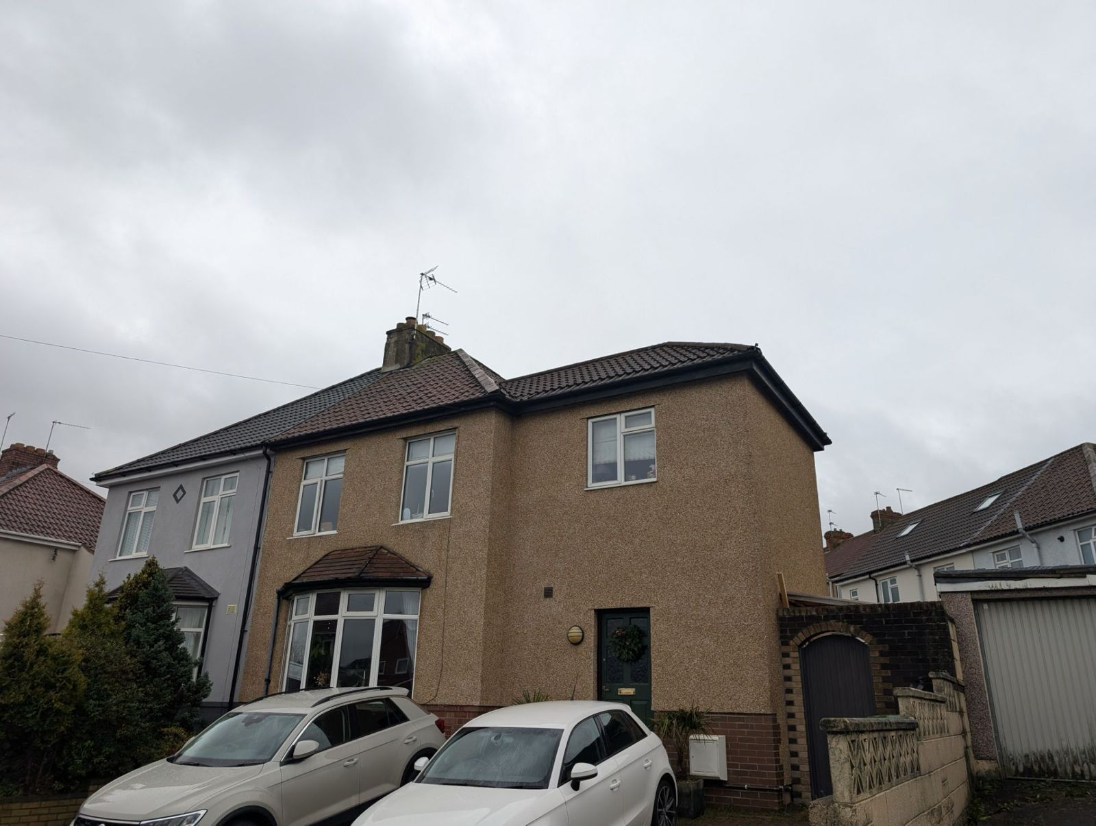 Suburban semi-detached house with parked cars under a cloudy sky