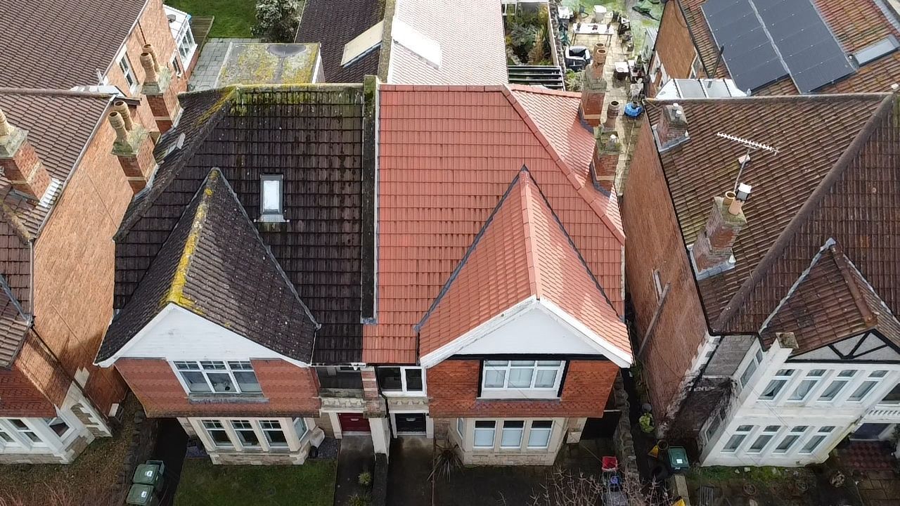 Aerial view of two brick houses with red roofs and a central dormer, surrounded by neighboring homes.