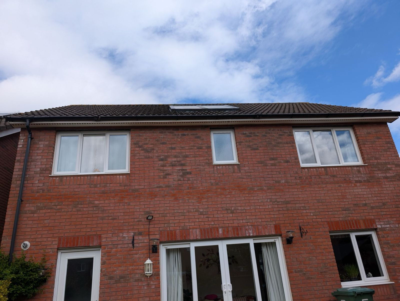 Two-story red-brick house with white windows and a cloudy blue sky above