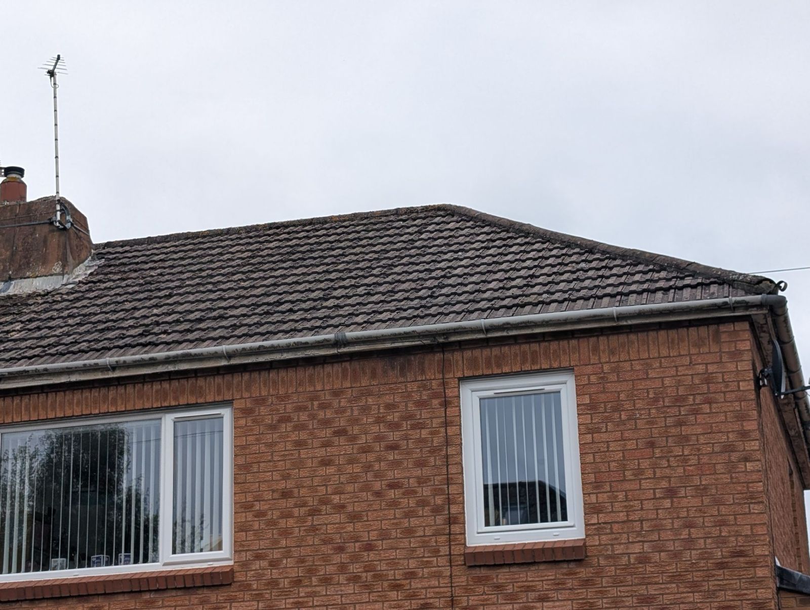Brick house with dark tiled roof and two front windows against a cloudy sky
