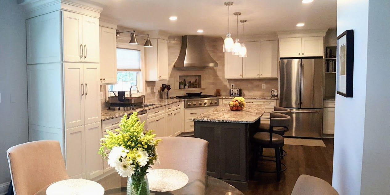 A kitchen with white cabinets and stainless steel appliances and a dining room with a table and chairs.