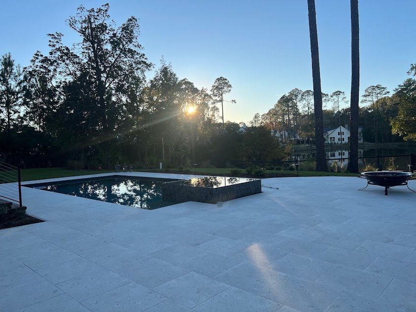 A large swimming pool in a backyard with the sun shining through the trees