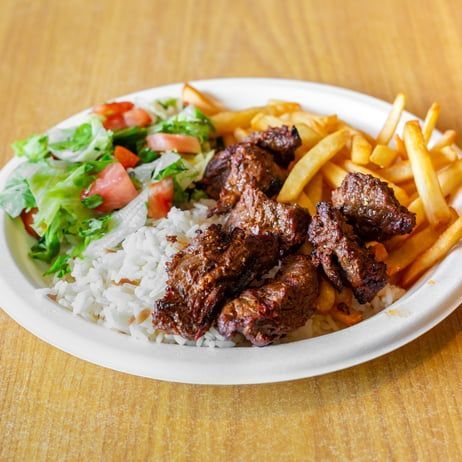 A plate of steak tips, white rice, French fries, and a side salad on a wooden table.